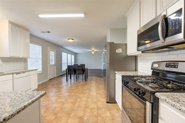 kitchen with decorative backsplash, light tile patterned floors, light stone counters, white cabinetry, and stainless steel appliances