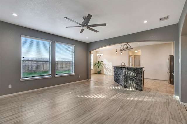 unfurnished living room featuring a textured ceiling, ceiling fan with notable chandelier, light hardwood / wood-style floors, and sink