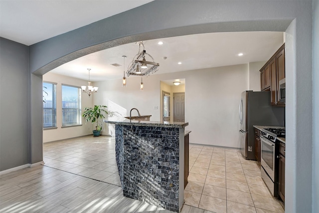 kitchen featuring stainless steel gas range, a notable chandelier, pendant lighting, dark brown cabinets, and light wood-type flooring