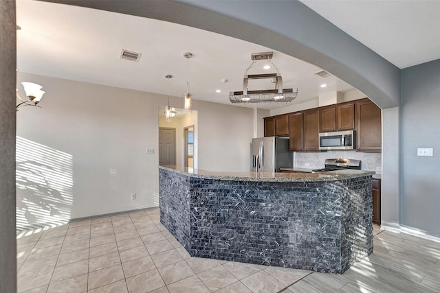 kitchen with a center island, pendant lighting, dark stone counters, dark brown cabinets, and appliances with stainless steel finishes