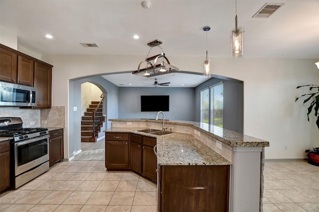 kitchen with light stone countertops, appliances with stainless steel finishes, sink, decorative light fixtures, and an island with sink