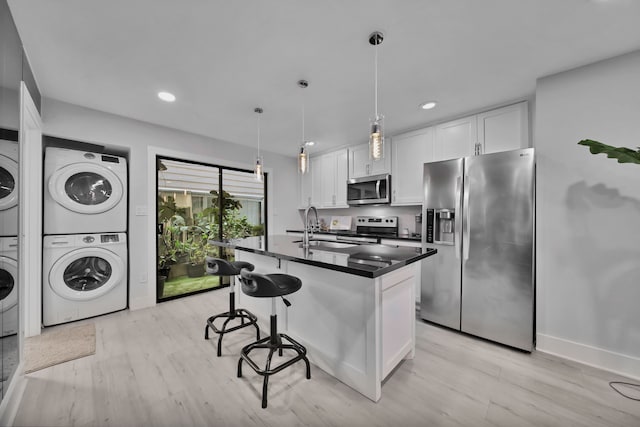 kitchen with sink, stacked washing maching and dryer, stainless steel appliances, light hardwood / wood-style floors, and white cabinets