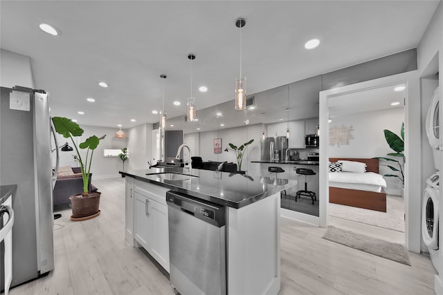 kitchen with sink, stainless steel appliances, stacked washer / drying machine, a center island with sink, and light wood-type flooring