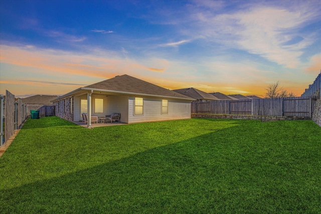 back house at dusk featuring a patio area and a yard