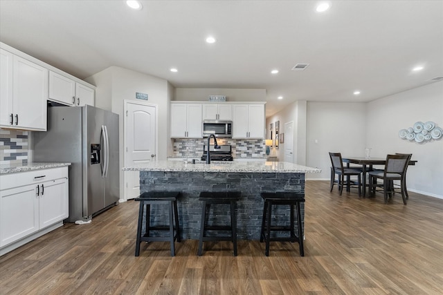 kitchen with an island with sink, stainless steel appliances, light stone countertops, white cabinets, and dark hardwood / wood-style floors