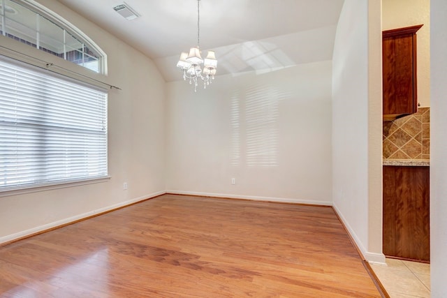 unfurnished room with vaulted ceiling, an inviting chandelier, and light hardwood / wood-style floors