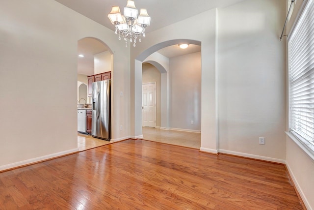 spare room with an inviting chandelier, sink, and light wood-type flooring