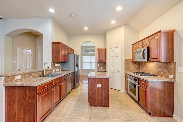 kitchen featuring sink, a center island, appliances with stainless steel finishes, kitchen peninsula, and light stone countertops