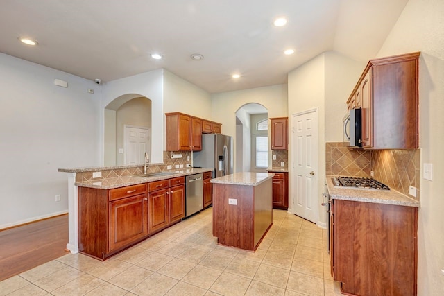 kitchen with sink, kitchen peninsula, a kitchen island, stainless steel appliances, and light stone countertops