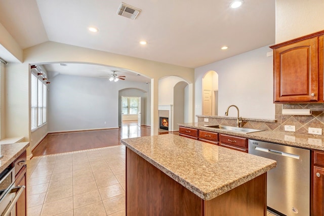 kitchen with sink, tasteful backsplash, light stone counters, stainless steel dishwasher, and a kitchen island