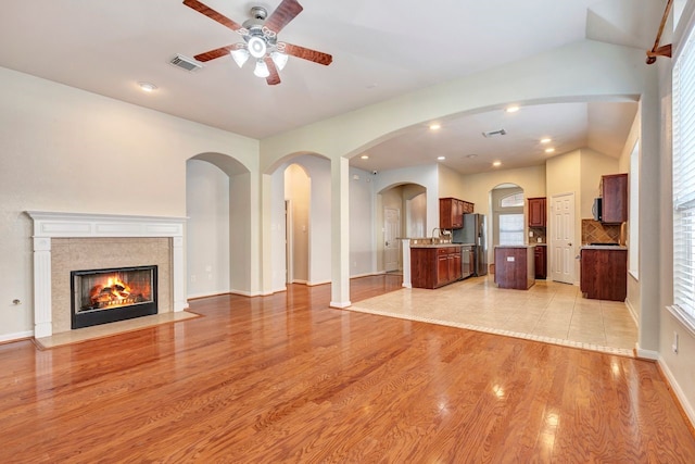 unfurnished living room with sink, vaulted ceiling, light wood-type flooring, ceiling fan, and a fireplace