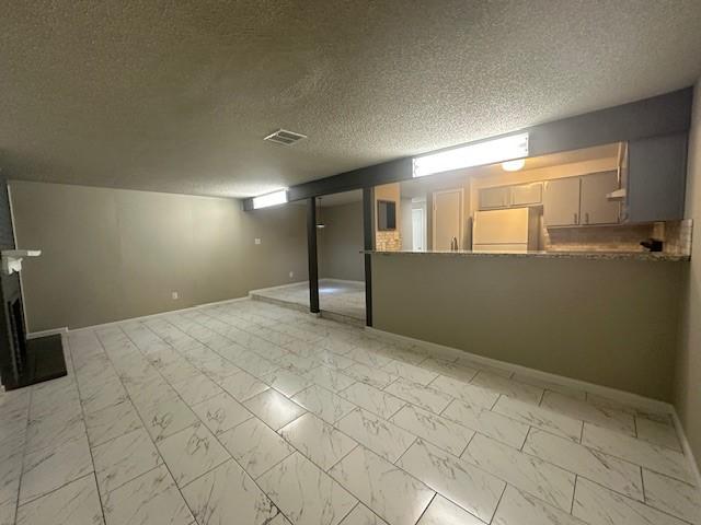 basement with a textured ceiling and white refrigerator