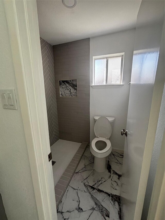 bathroom featuring tiled shower and toilet