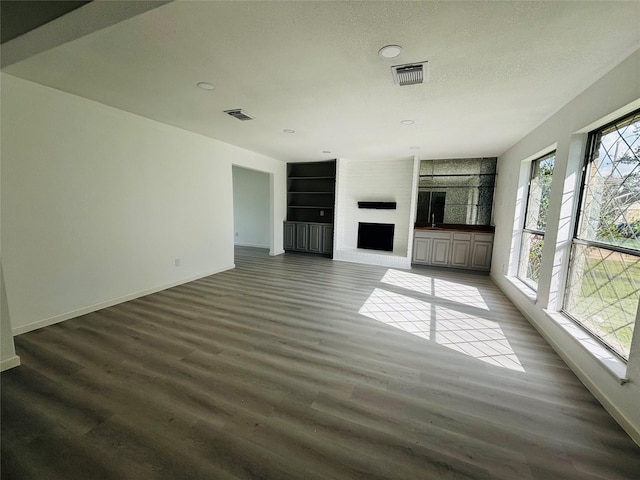 unfurnished living room featuring a large fireplace, dark hardwood / wood-style floors, and built in features