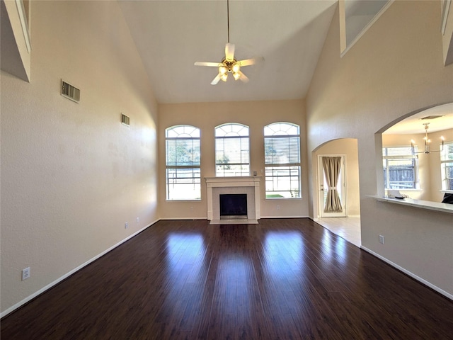 unfurnished living room with ceiling fan with notable chandelier, high vaulted ceiling, and dark wood-type flooring