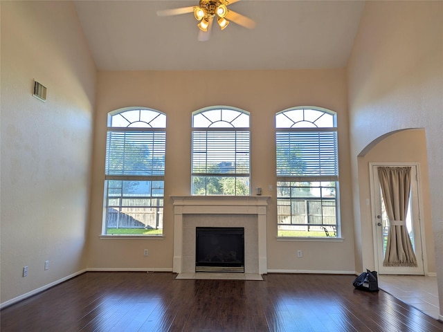 unfurnished living room featuring ceiling fan, a healthy amount of sunlight, dark hardwood / wood-style flooring, and a fireplace