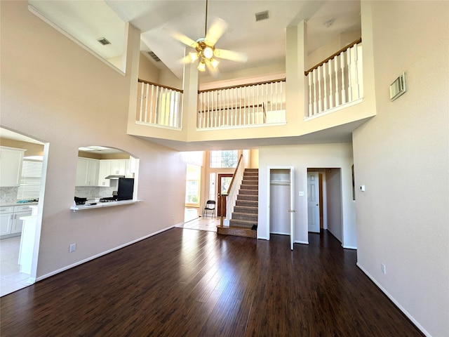 unfurnished living room featuring a high ceiling, ceiling fan, and dark wood-type flooring