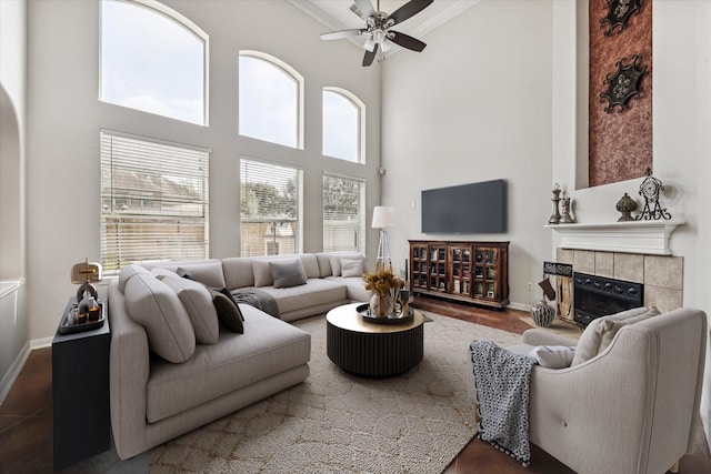 living room featuring ceiling fan, dark hardwood / wood-style flooring, crown molding, a towering ceiling, and a tiled fireplace