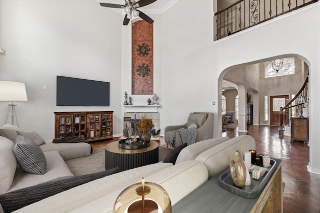 living room with a towering ceiling, ornamental molding, ceiling fan, a tile fireplace, and dark hardwood / wood-style floors