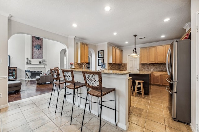 kitchen with light stone countertops, a kitchen bar, kitchen peninsula, stainless steel refrigerator, and a tiled fireplace