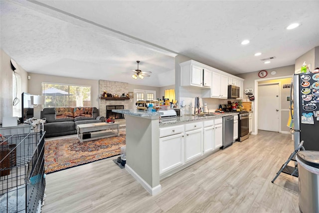 kitchen featuring white cabinets, a textured ceiling, stainless steel appliances, and a brick fireplace