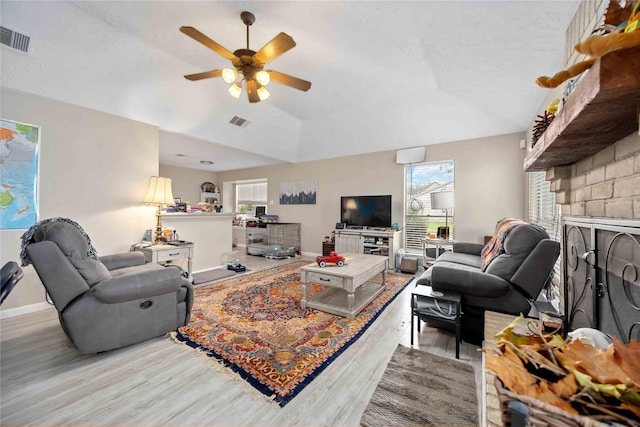 living room with a brick fireplace, ceiling fan, a textured ceiling, and light hardwood / wood-style flooring