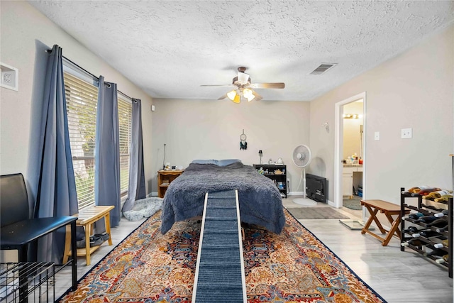 bedroom with ceiling fan, ensuite bathroom, a textured ceiling, and light hardwood / wood-style flooring