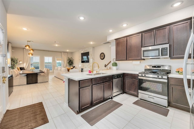 kitchen featuring sink, kitchen peninsula, pendant lighting, dark brown cabinets, and appliances with stainless steel finishes