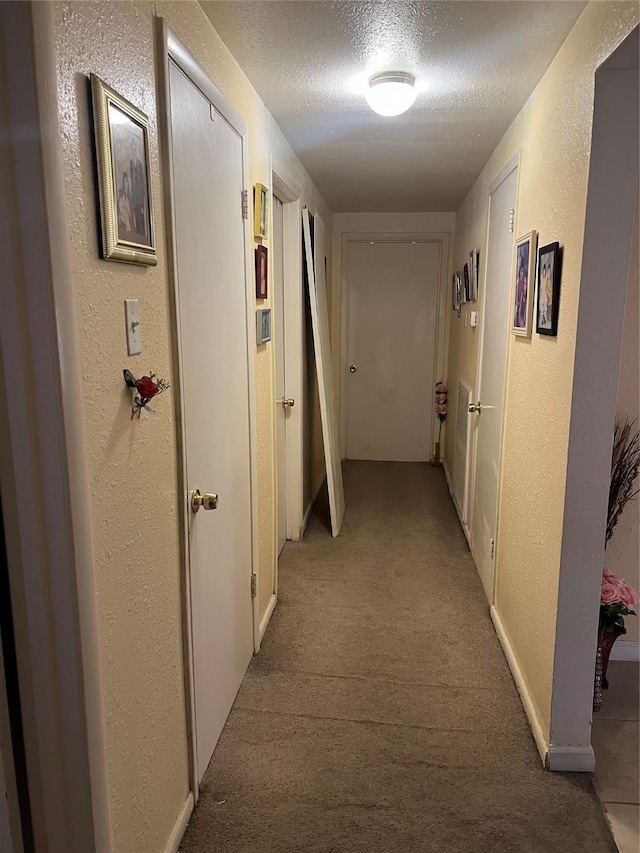 hallway with a textured ceiling, a textured wall, and light colored carpet