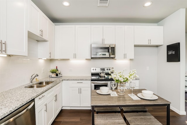 kitchen with sink, dark hardwood / wood-style floors, light stone countertops, appliances with stainless steel finishes, and white cabinetry