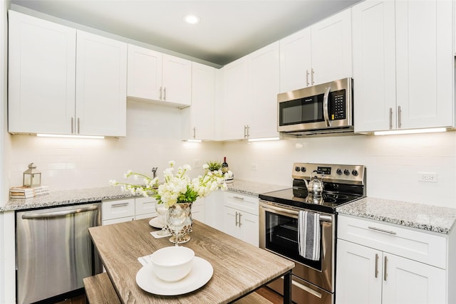 kitchen with white cabinets, light stone countertops, stainless steel appliances, and tasteful backsplash