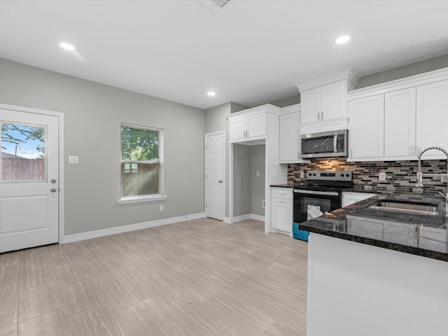 kitchen featuring appliances with stainless steel finishes, backsplash, sink, dark stone countertops, and white cabinets