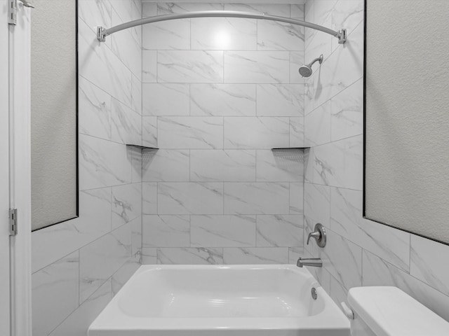 bathroom featuring toilet, tiled shower / bath, and tile walls