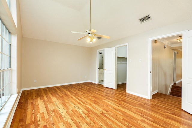 unfurnished bedroom with crown molding, light hardwood / wood-style flooring, ceiling fan, a spacious closet, and a closet