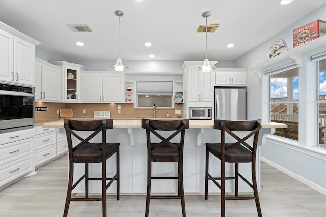 kitchen with pendant lighting, a breakfast bar, white cabinetry, and appliances with stainless steel finishes