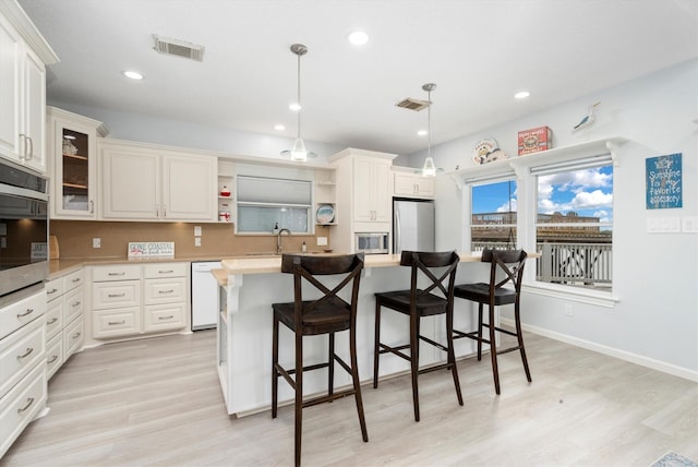 kitchen featuring a center island, light hardwood / wood-style floors, decorative light fixtures, a breakfast bar area, and appliances with stainless steel finishes