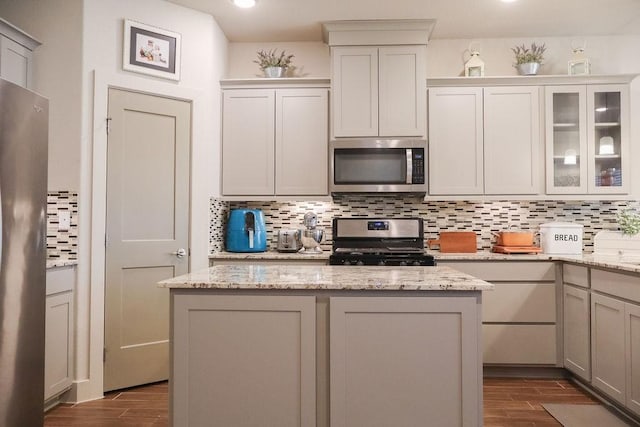 kitchen with light stone countertops, wood-type flooring, appliances with stainless steel finishes, and tasteful backsplash