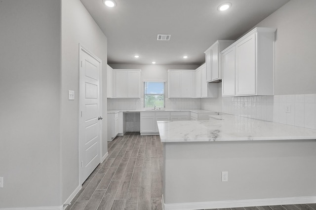 kitchen with kitchen peninsula, light wood-type flooring, tasteful backsplash, sink, and white cabinetry