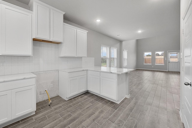 kitchen with tasteful backsplash, kitchen peninsula, white cabinetry, and light wood-type flooring