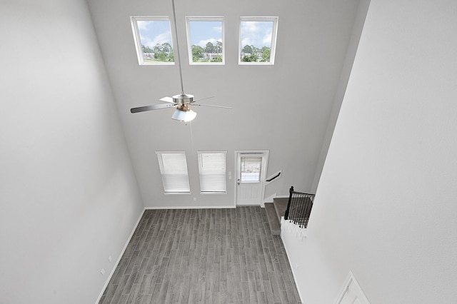 unfurnished living room with ceiling fan, light wood-type flooring, a wealth of natural light, and a towering ceiling