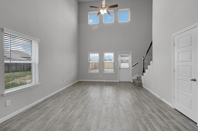 unfurnished living room with ceiling fan, light hardwood / wood-style floors, and a high ceiling