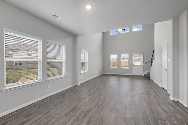 unfurnished living room with a towering ceiling, a wealth of natural light, and dark wood-type flooring