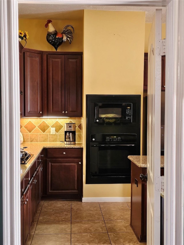 kitchen featuring light tile patterned flooring, backsplash, light stone counters, and black appliances