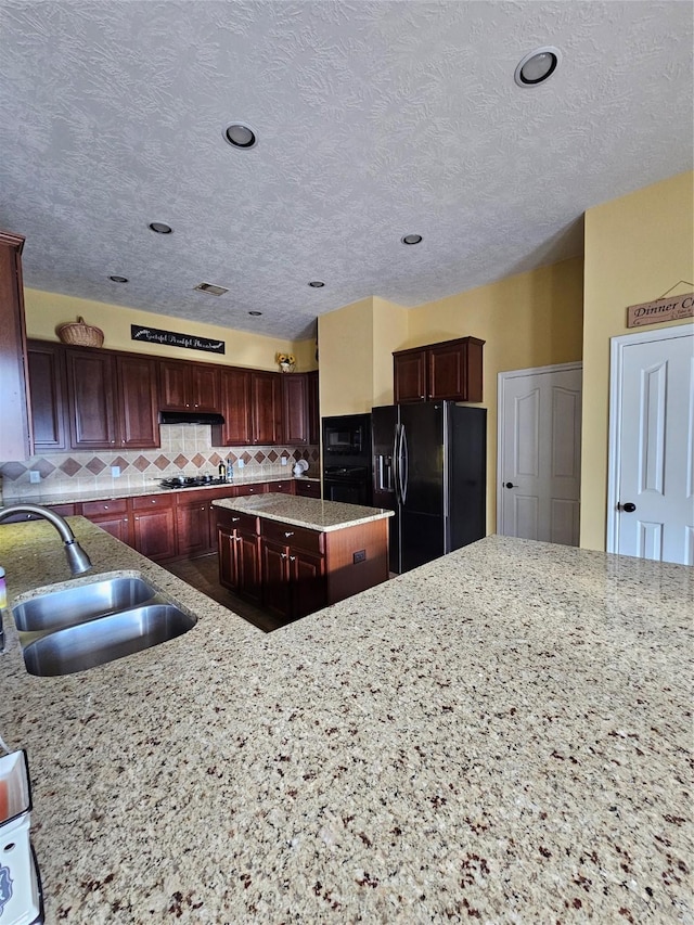 kitchen with decorative backsplash, light stone counters, sink, black appliances, and a center island