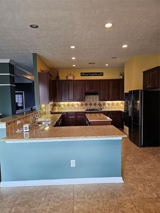 kitchen with kitchen peninsula, black refrigerator with ice dispenser, sink, and light stone countertops