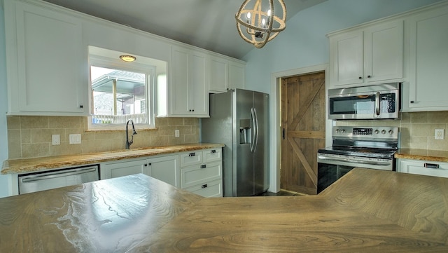 kitchen featuring vaulted ceiling, pendant lighting, sink, white cabinetry, and stainless steel appliances