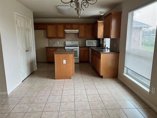 kitchen with decorative backsplash, white appliances, sink, light tile patterned floors, and a kitchen island