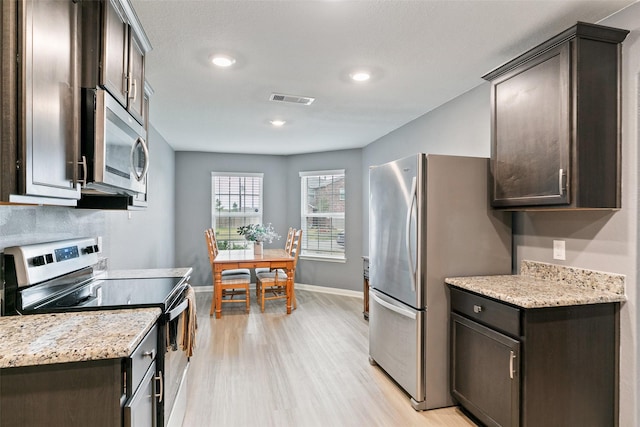 kitchen featuring appliances with stainless steel finishes, dark brown cabinetry, light hardwood / wood-style floors, and light stone counters