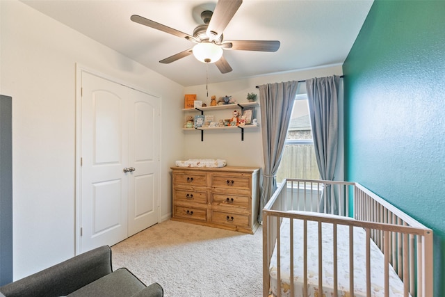 carpeted bedroom featuring ceiling fan and a crib