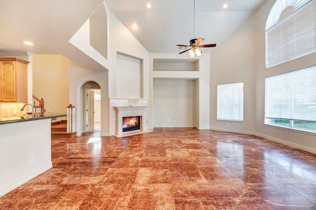 unfurnished living room featuring built in shelves, ceiling fan, sink, high vaulted ceiling, and a fireplace